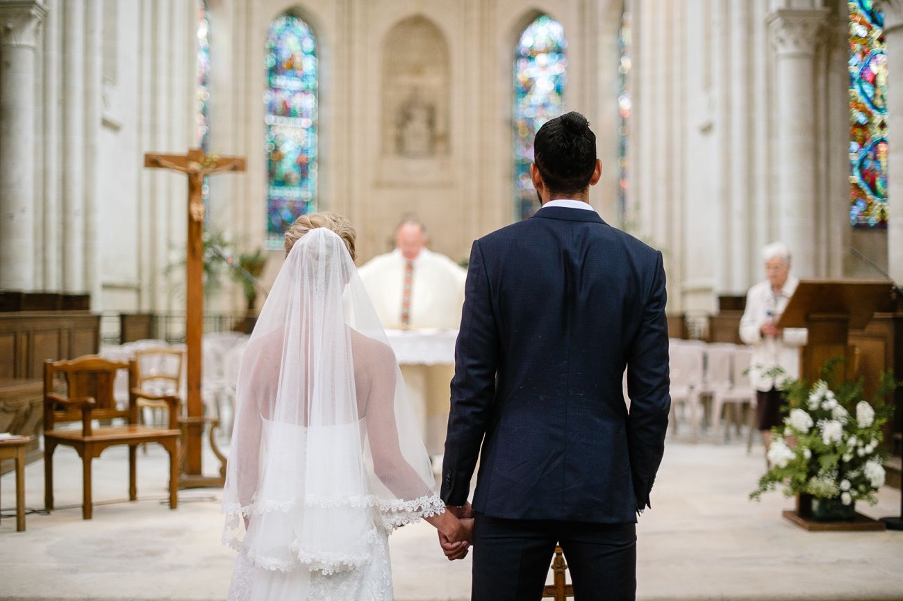 Bride and groom holding hands at the altar during a church wedding ceremony with a priest officiating.