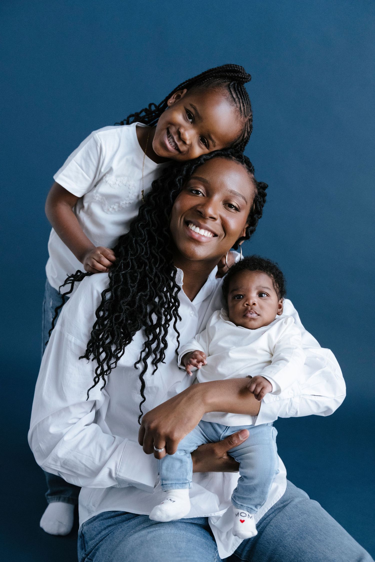 A joyful mother poses with her two young children against a deep blue background in matching outfits.