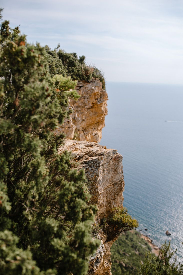 Rocky coastal cliff with green shrubs overlooking calm blue Mediterranean sea.