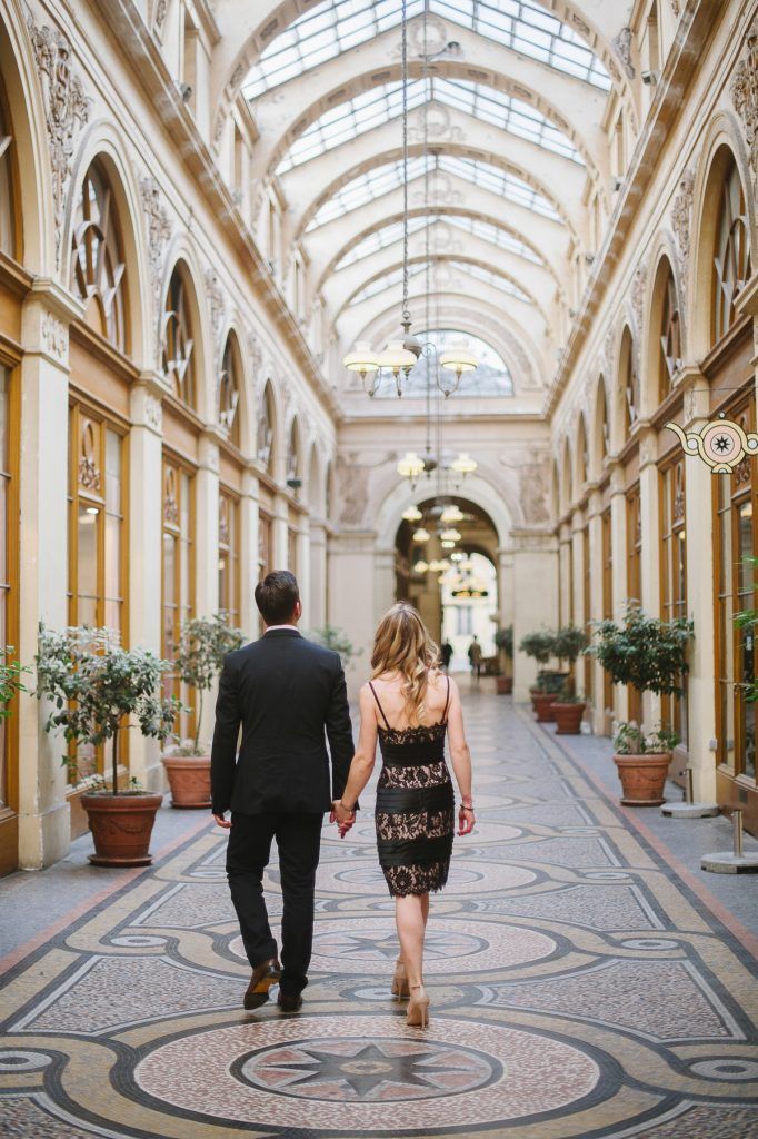 Elegant couple walking hand-in-hand through the stunning glass-roofed arcade of Galerie Vivienne in Paris.