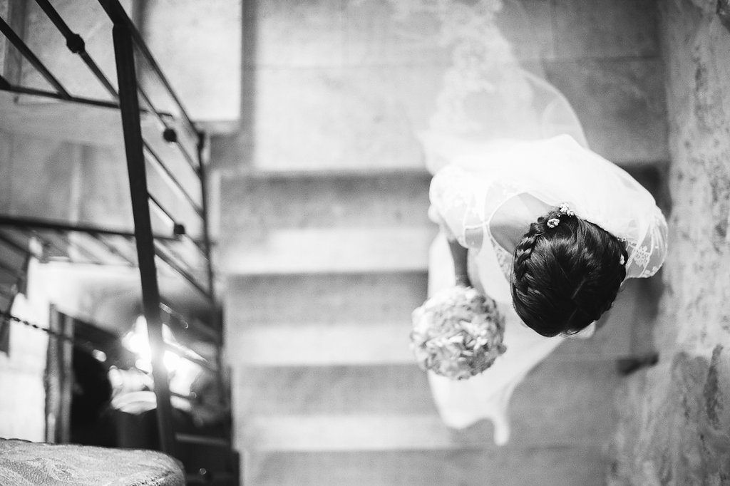 Artistic overhead black and white shot of bride descending stone staircase with bouquet.