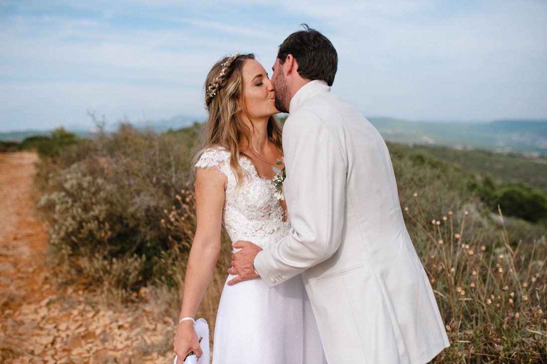Bride and groom sharing a romantic kiss outdoors on their wedding day with scenic hills in the background.