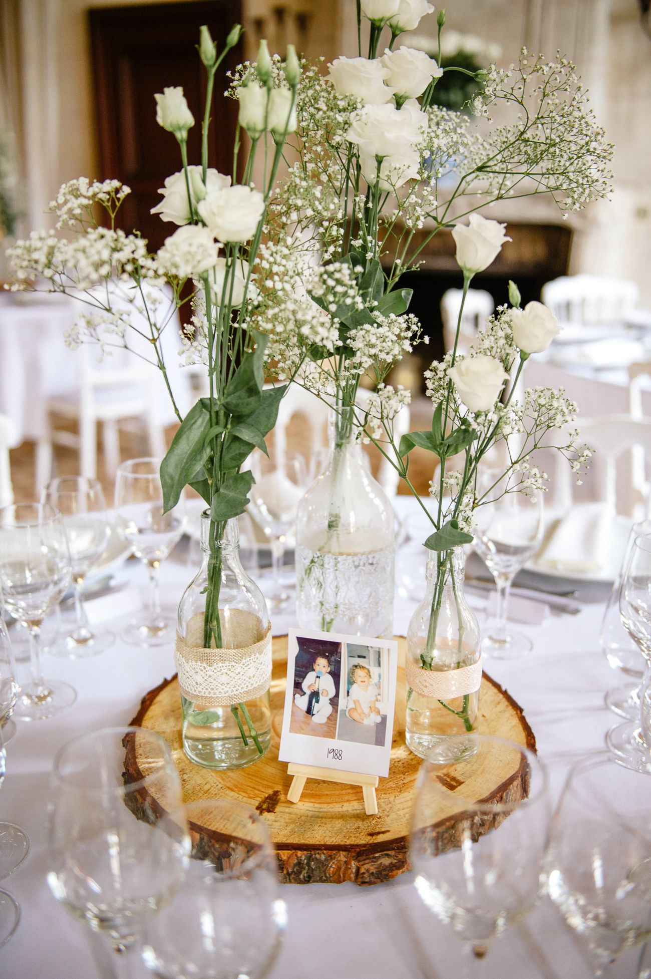 Rustic wedding centerpiece with white roses and baby's breath in glass vases on a wood slice.