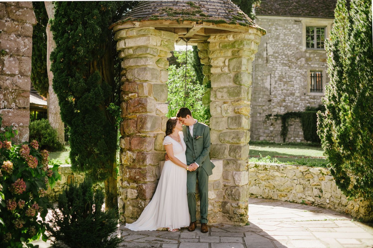 Bride and groom sharing an intimate moment under a stone archway in a lush garden wedding venue.