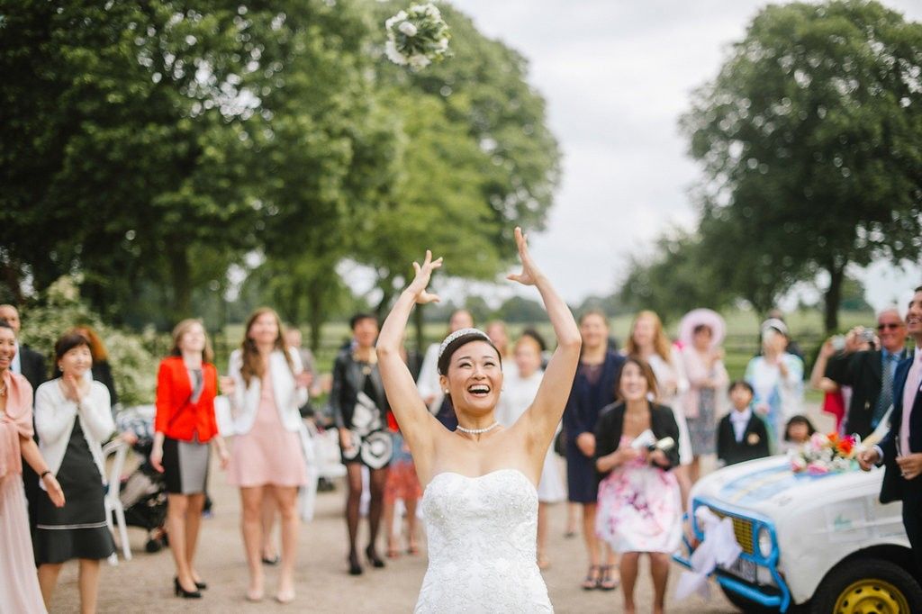 Joyful bride in white gown tossing bouquet to guests at outdoor wedding celebration.
