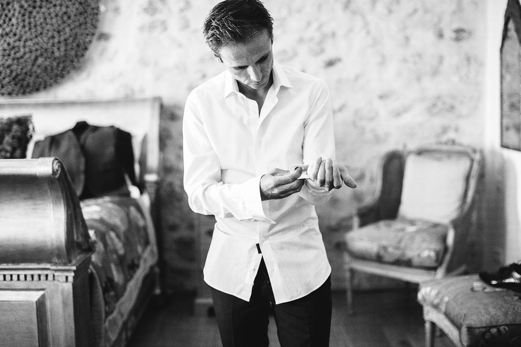 Black and white photo of groom in white shirt adjusting cufflinks before wedding.