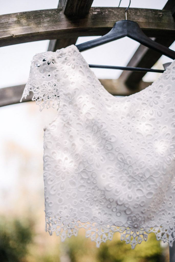Elegant white lace bridal crop top hanging on wooden pergola hanger outdoors.
