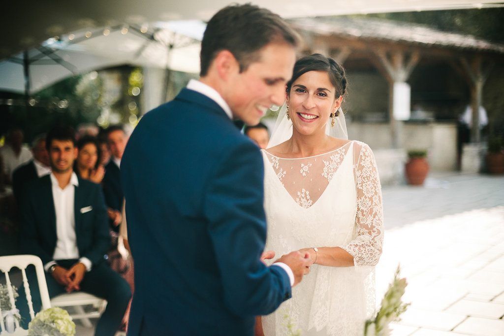 Radiant bride gazing lovingly at groom during ring exchange at sunny outdoor wedding ceremony.