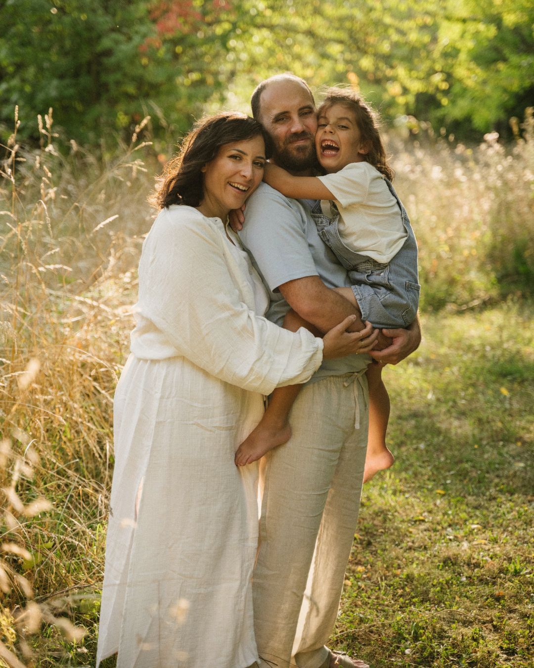 Happy family with laughing child embracing in golden sunlit meadow.