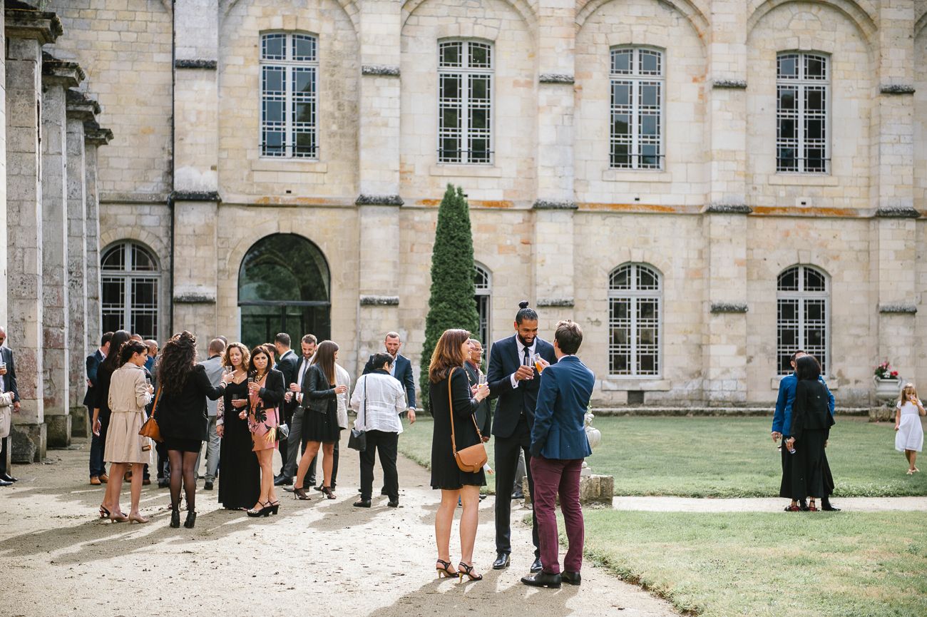 Wedding guests mingling outdoors in front of an elegant French chateau on a sunny day.
