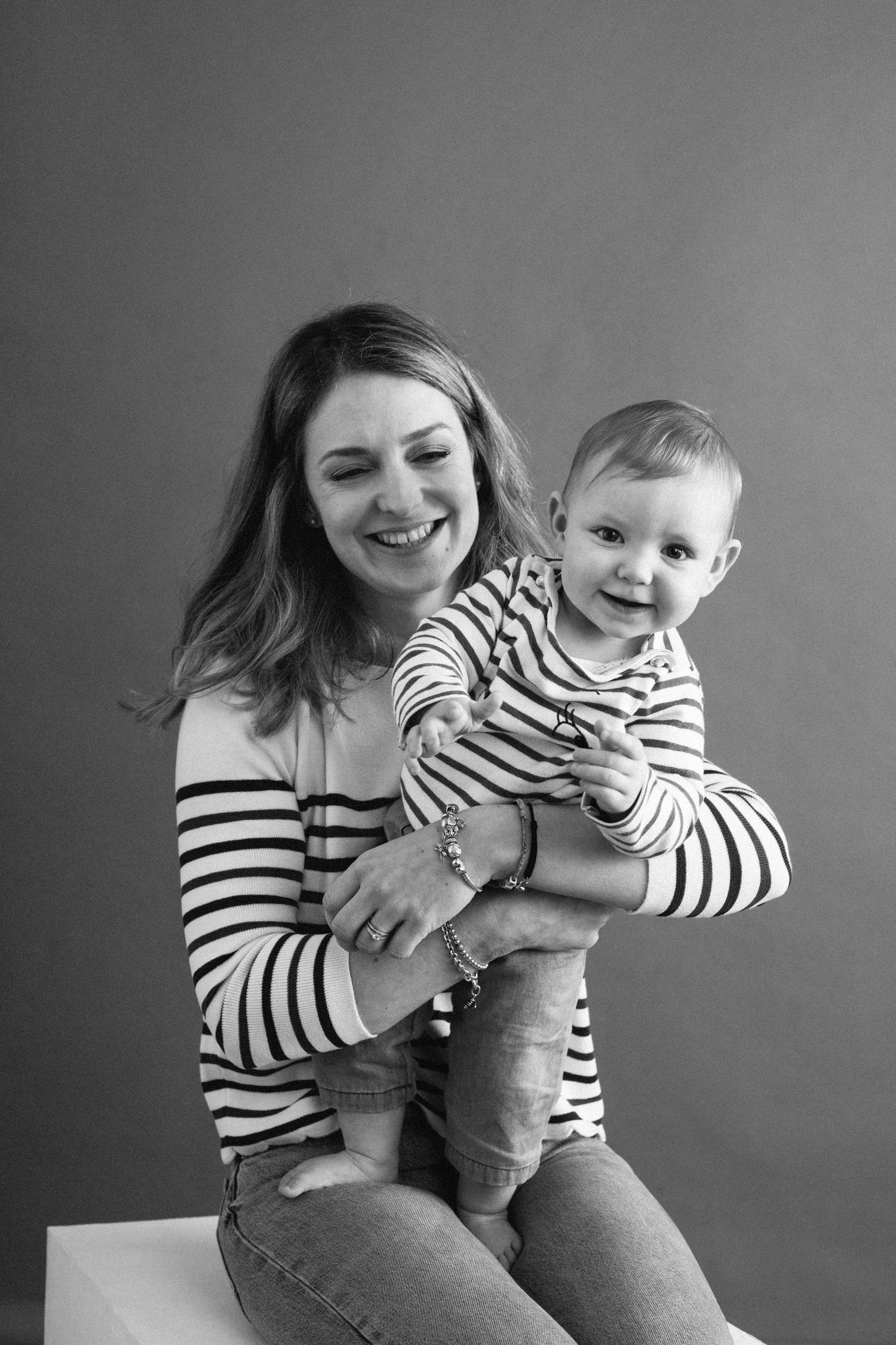 A smiling mother and baby in matching striped shirts pose together in a black and white portrait.