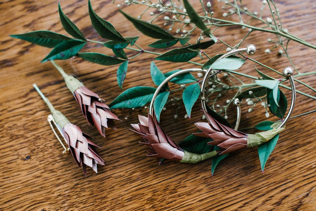 Wedding accessories flat lay with silver hoop earrings, leaf earrings, and greenery.