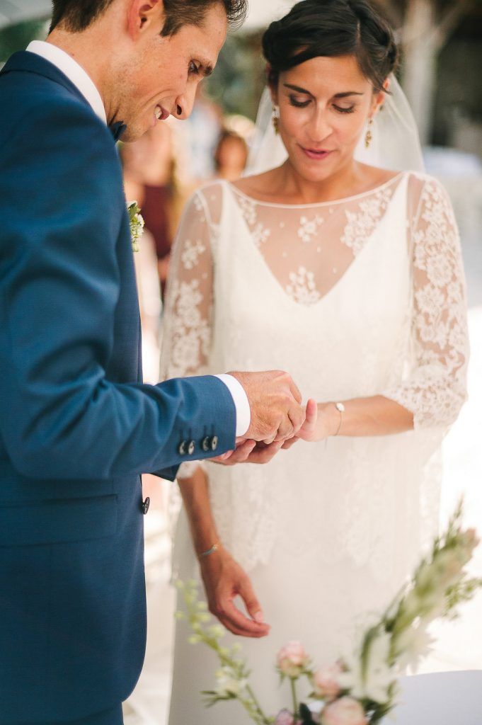 Groom carefully placing wedding ring on brides finger as she watches during outdoor ceremony.