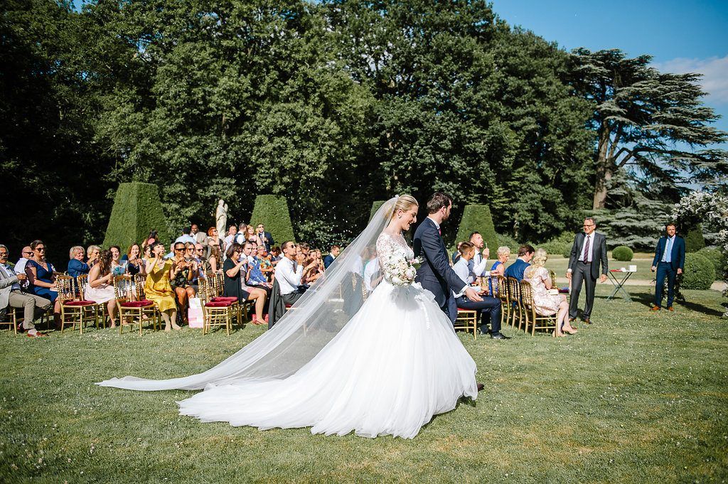 Bride and groom share romantic kiss on sun-drenched lawn during outdoor garden wedding reception.