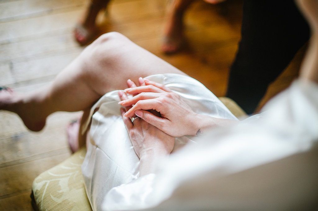 Close-up of bride in white satin robe with hands resting on lap on wedding morning.