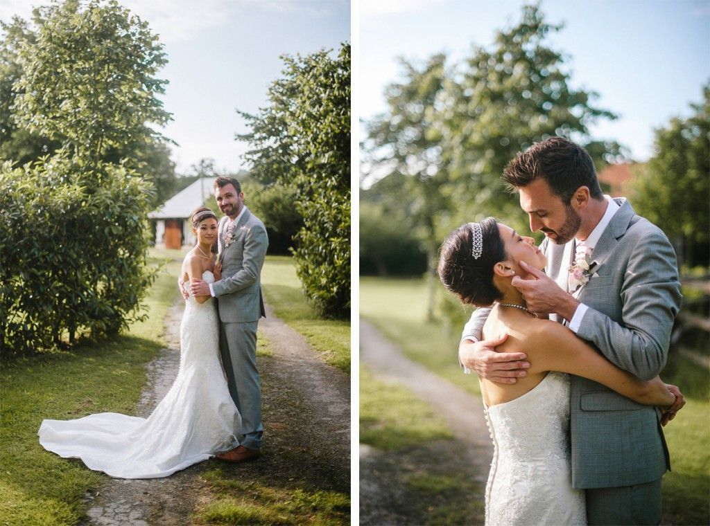 Bride and groom share tender embrace on garden path at sunny outdoor wedding.