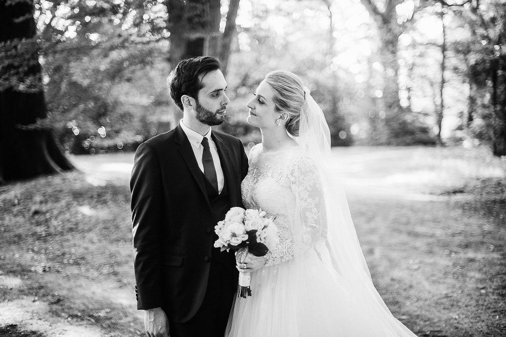 Groom kissing bride on cheek in romantic black and white woodland wedding portrait.