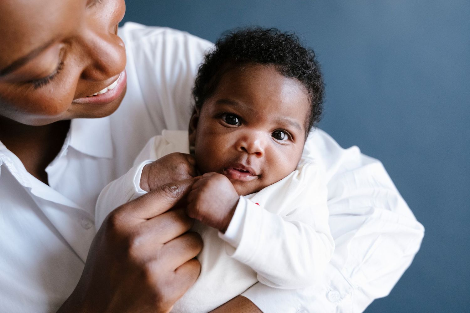 Mother smiling while holding newborn baby against gray background.