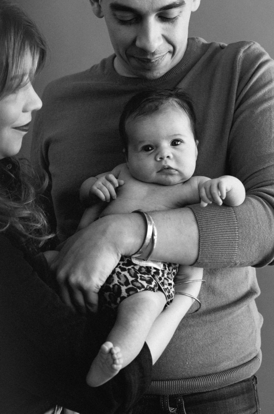 Parents lovingly cradle their newborn baby in a black and white intimate family portrait.