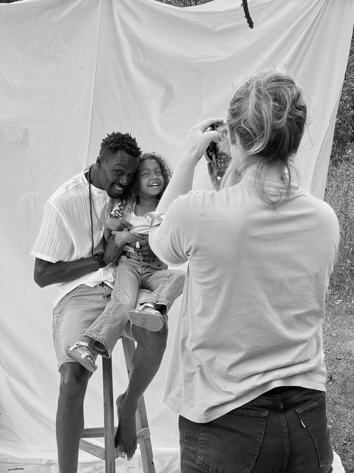 Black and white photo of a photographer capturing a portrait of a father and daughter against a white backdrop.