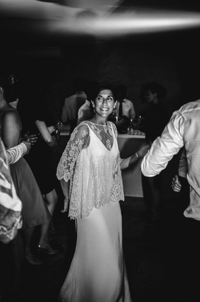 Bride in elegant lace cape wedding dress smiling while dancing at wedding reception.