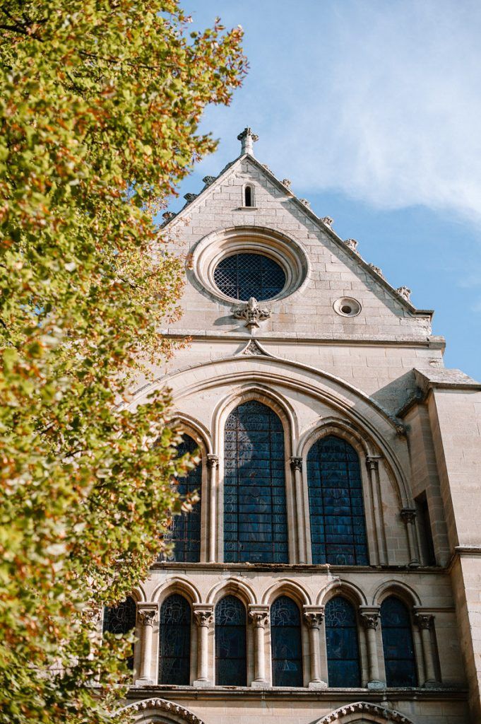 Gothic church facade with rose window and arched stained glass windows framed by autumn trees.