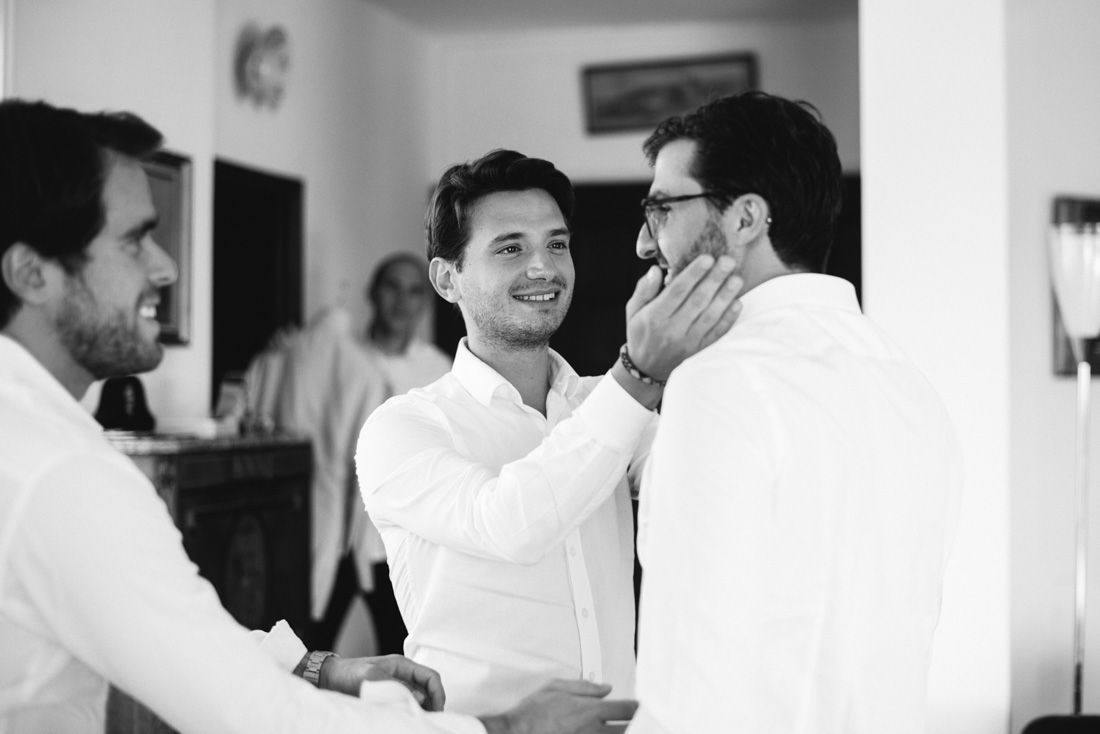 Black and white photo of groomsmen helping groom prepare before wedding ceremony.