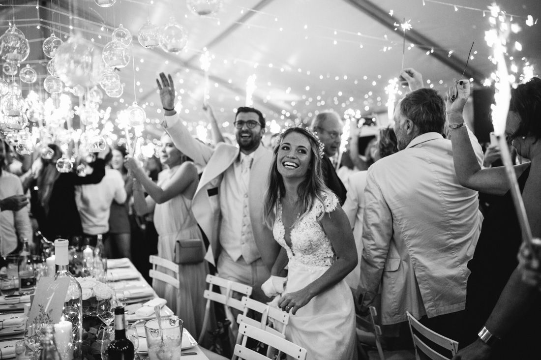 Bride smiles joyfully as guests celebrate with sparklers at an elegant wedding reception.