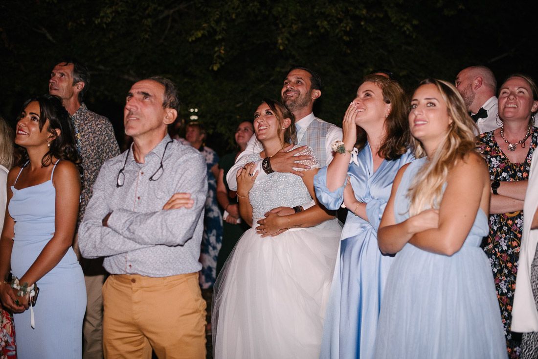 Wedding guests gazing upward in amazement during outdoor evening celebration at rustic venue.