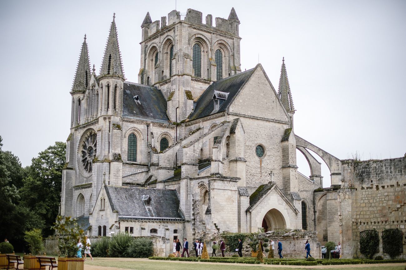 Gothic stone cathedral with tall spires surrounded by lush green gardens and wedding guests.