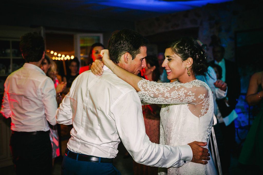 Bride in lace sleeve wedding dress dancing and smiling with groom at reception.