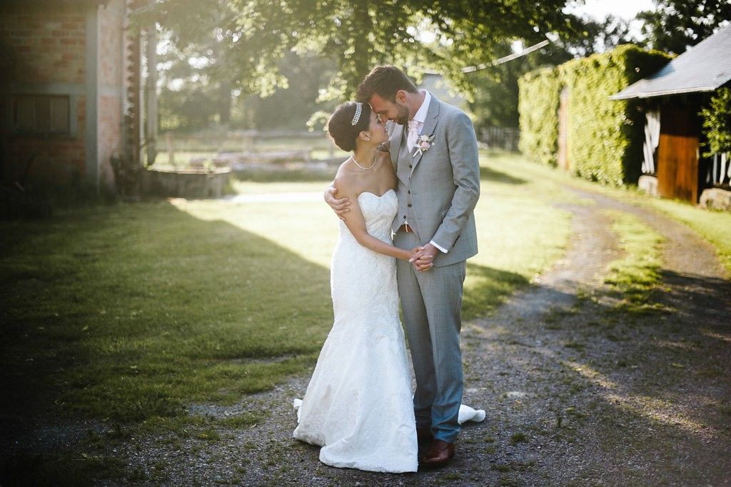 Newlyweds embracing and kissing outdoors in warm golden sunlight on their wedding day.
