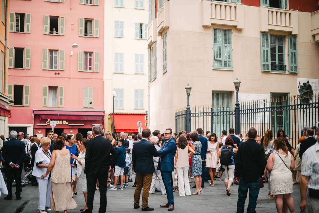 Wedding guests gather and mingle outside colorful Mediterranean buildings in the streets of Nice, France.