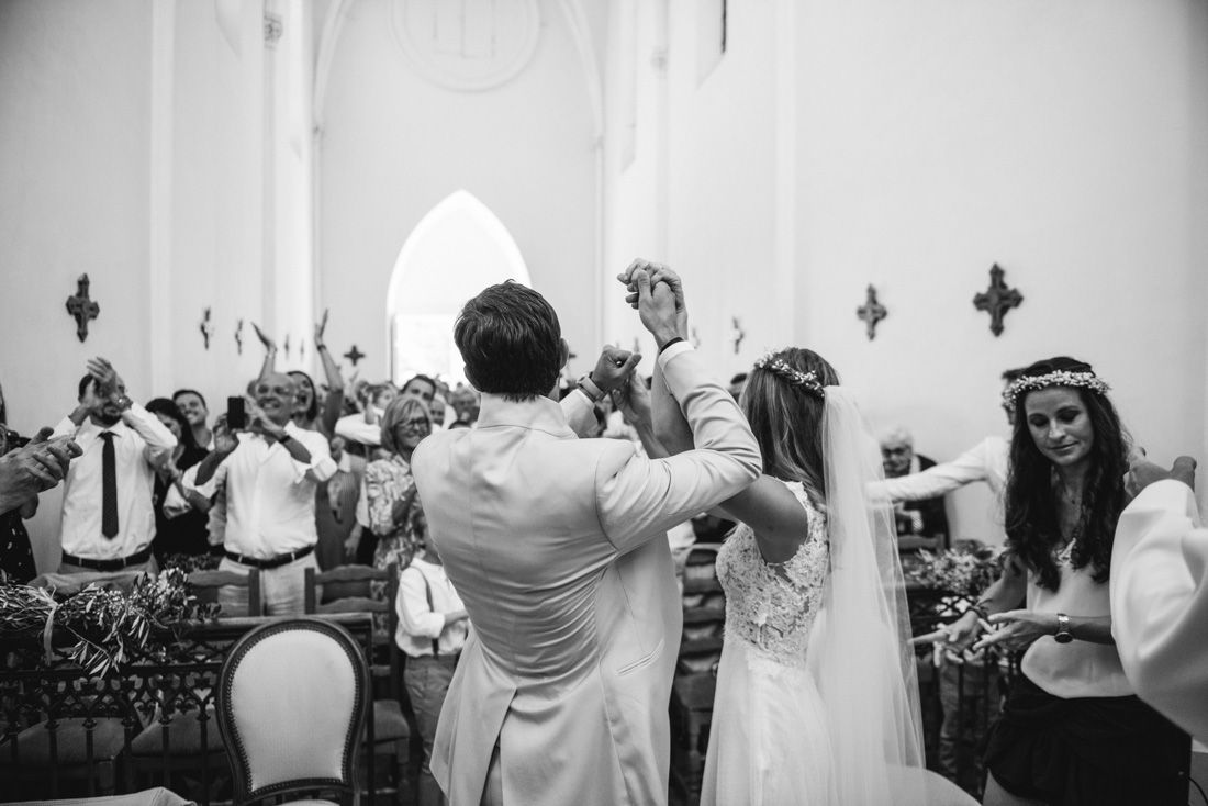 Bride and groom celebrate with raised hands among joyful guests in church ceremony.