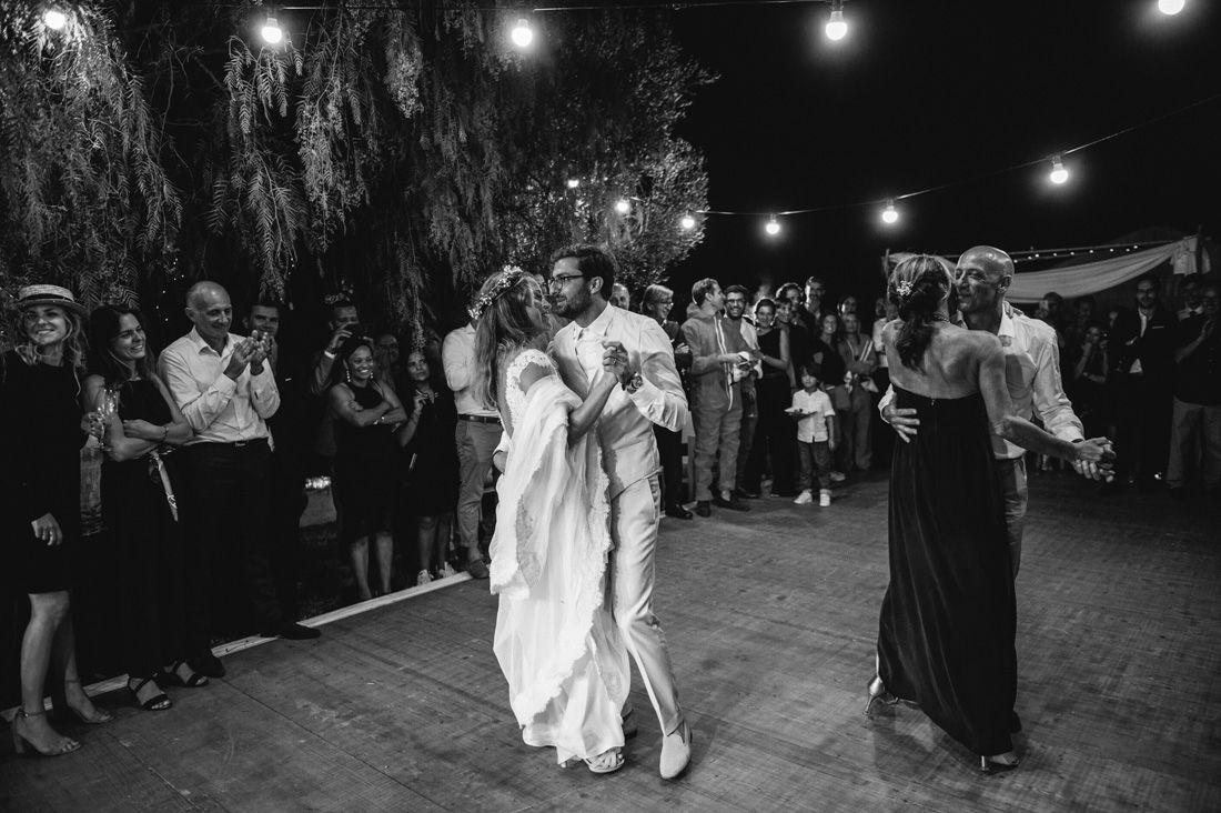 Black and white photo of a couple sharing their first dance at an outdoor wedding reception with guests watching.