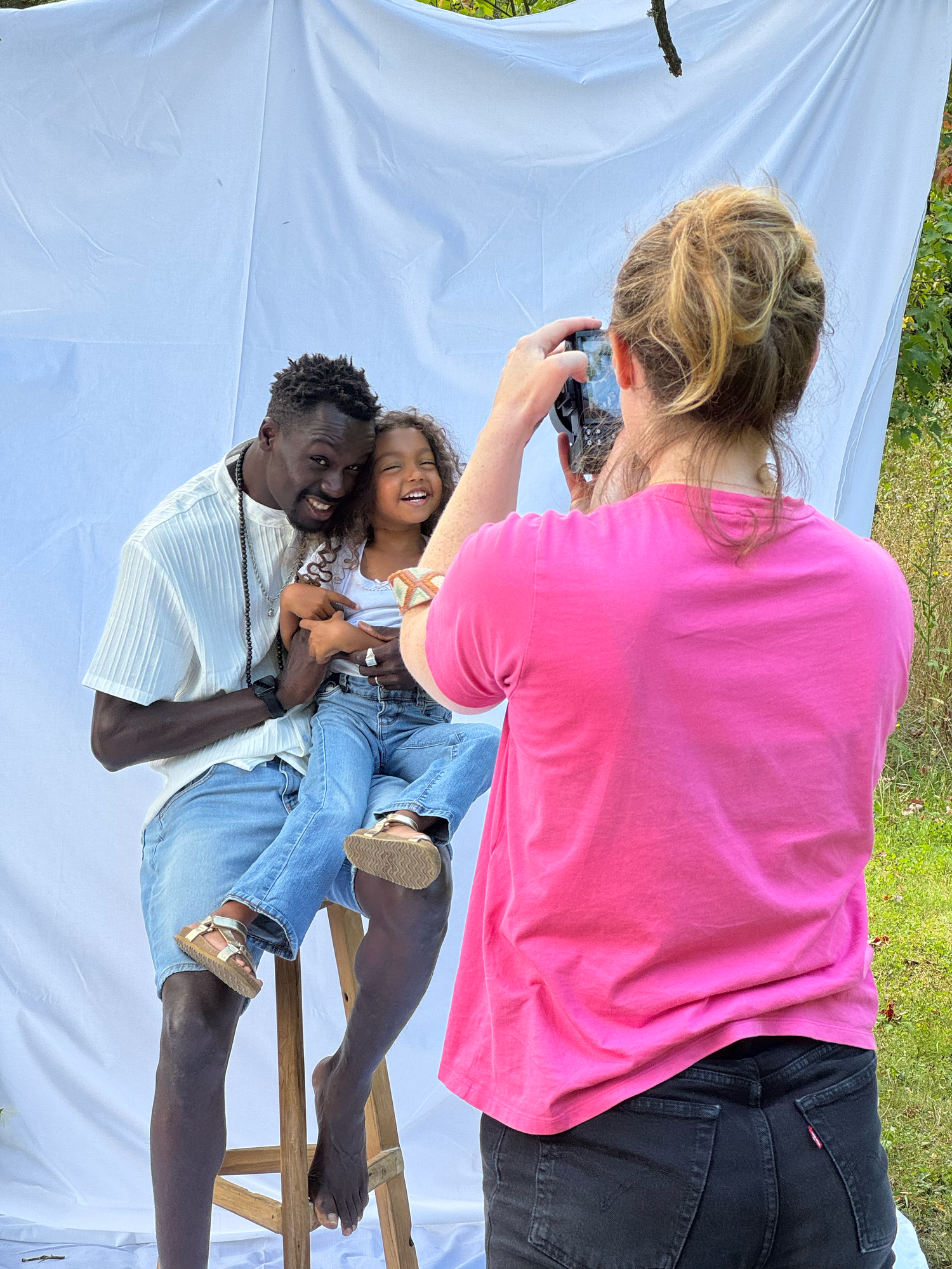 Female photographer capturing father and daughter during outdoor portrait session.