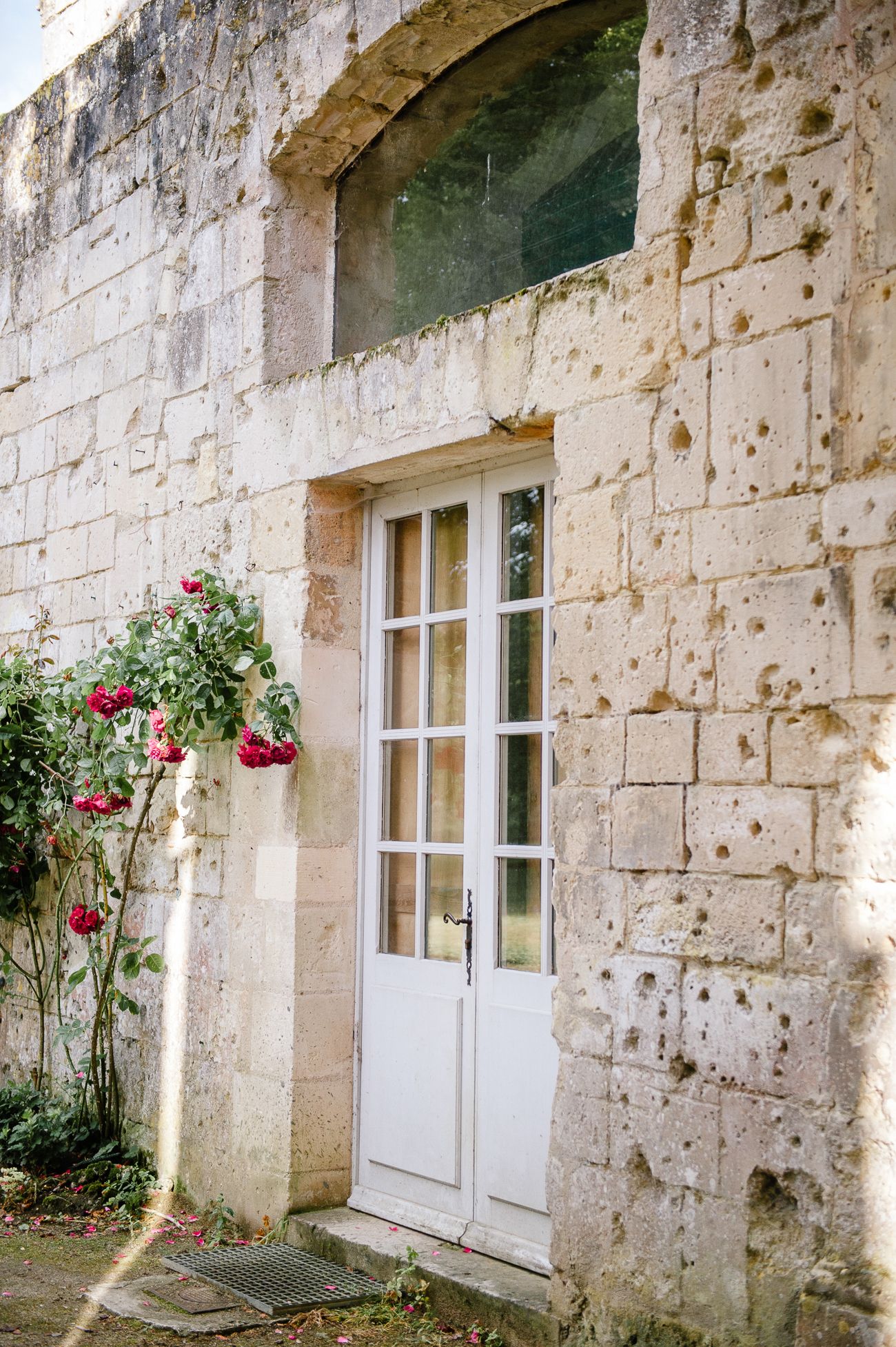 Rustic stone building exterior with white French door and climbing red rose bush in natural daylight.
