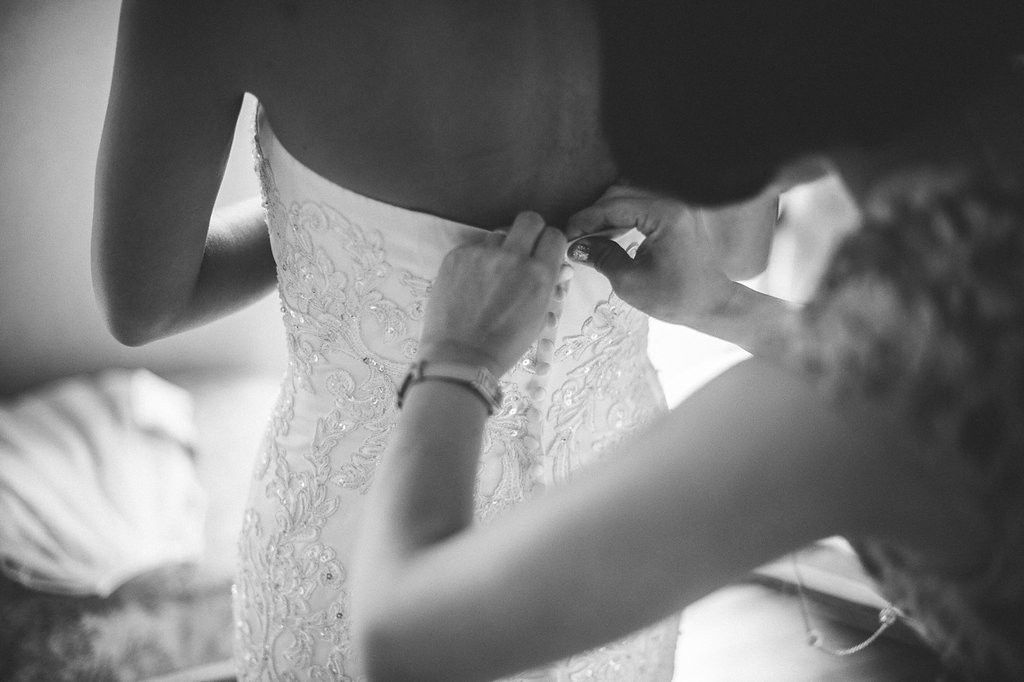 Close-up black and white image of delicate lace wedding dress buttons being fastened.
