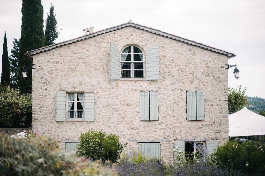 Rustic stone Provencal farmhouse with sage green shutters surrounded by lavender and cypress trees.