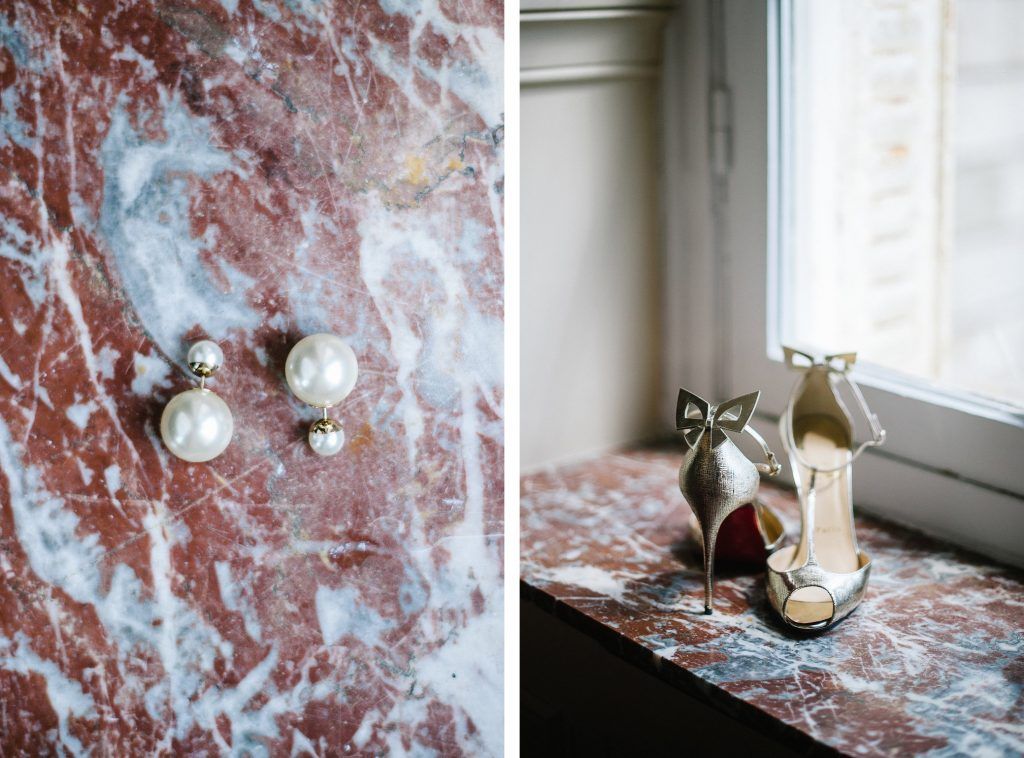 Wedding details featuring pearl drop earrings and gold bow Christian Louboutin heels on marble.