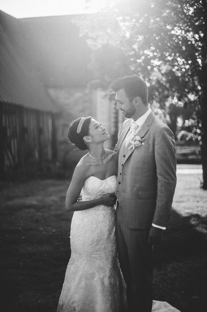 Black and white romantic portrait of bride and groom smiling at each other in warm sunlight.
