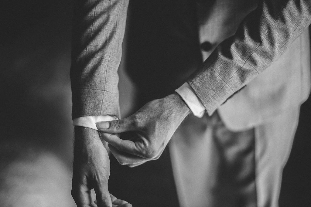 Black and white close-up of a groom adjusting his cufflinks on his suit sleeve before the wedding ceremony.