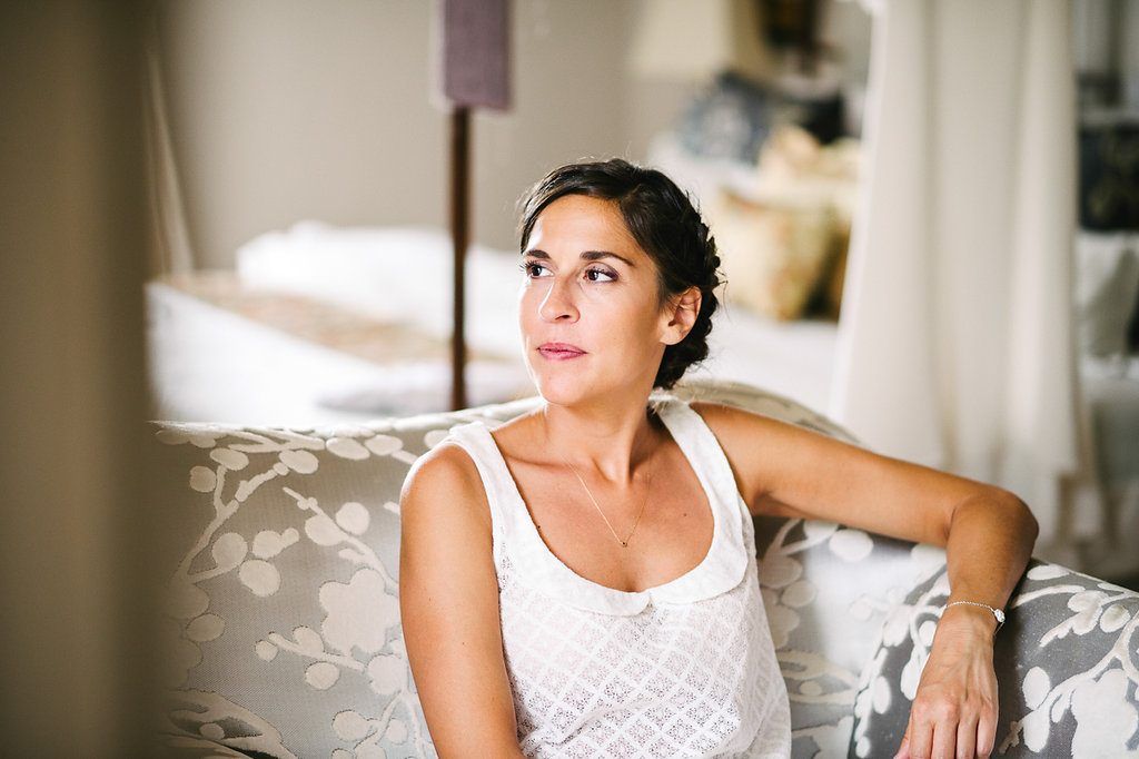 Beautiful brunette bride in white lace top relaxing on floral sofa before wedding.