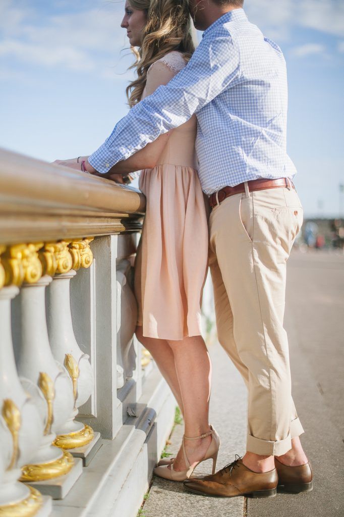Couple standing close together leaning on ornate golden railing of a Parisian bridge.