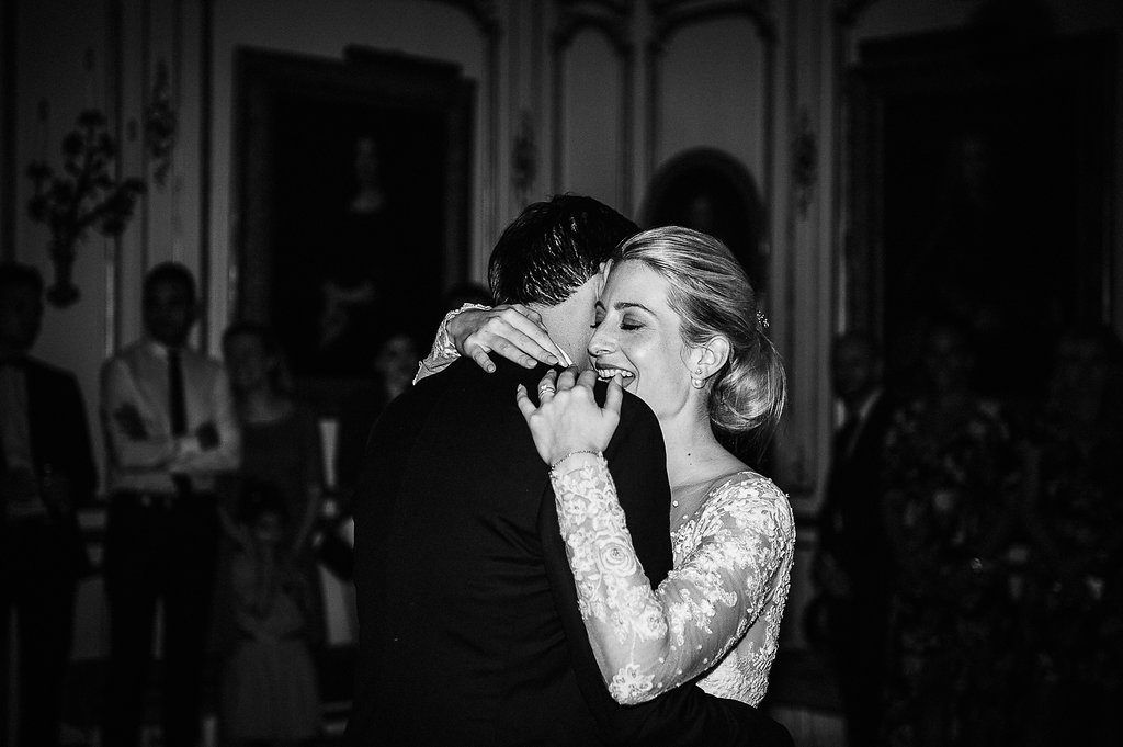 Emotional bride in lace wedding gown embraces groom during intimate first dance at French chateau wedding.