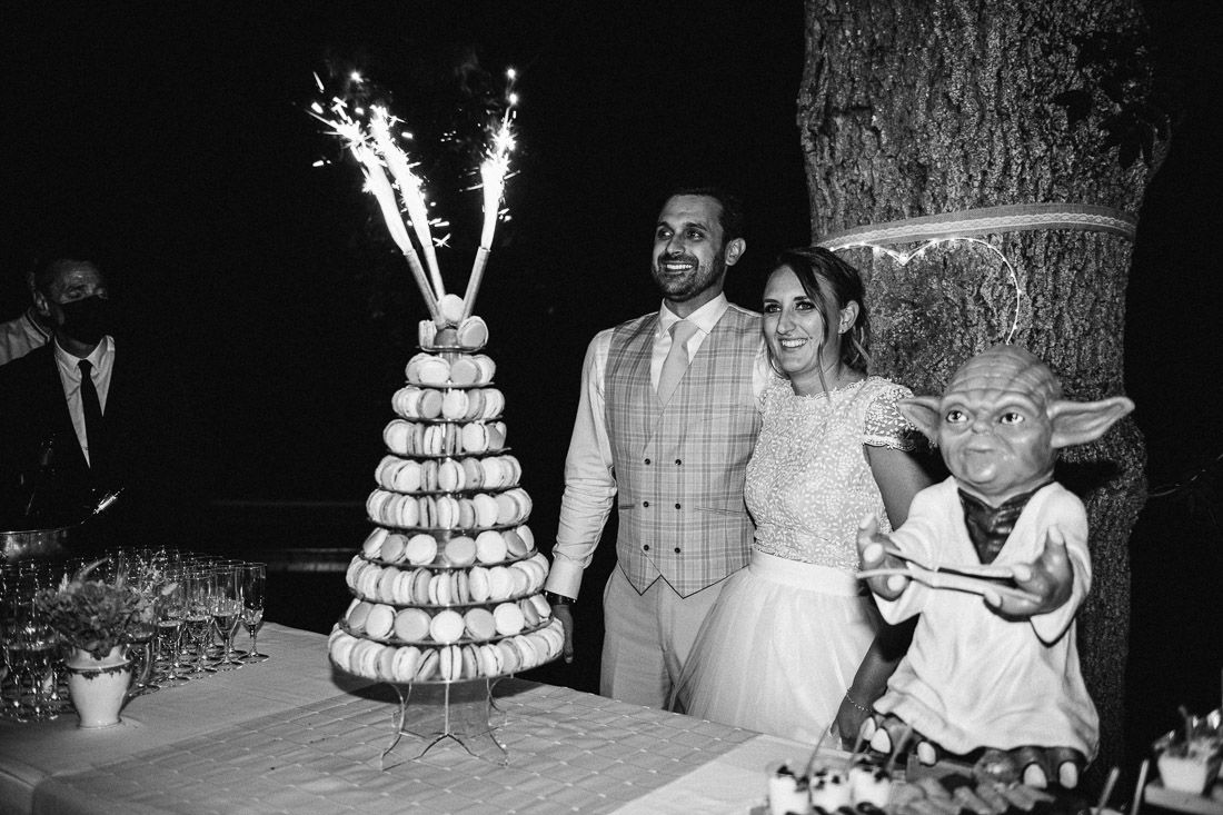 Bride and groom cut macaron tower wedding cake with sparklers and Yoda figurine in black and white.