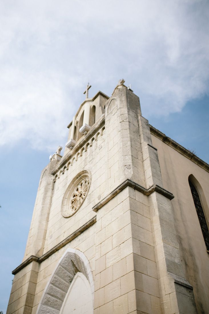 Historic stone church facade with arched windows, rose window, and cross atop bell tower against a blue sky.