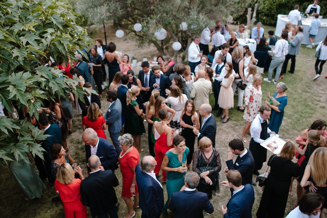 Aerial view of elegant outdoor wedding reception with guests mingling in garden setting, wearing formal attire.