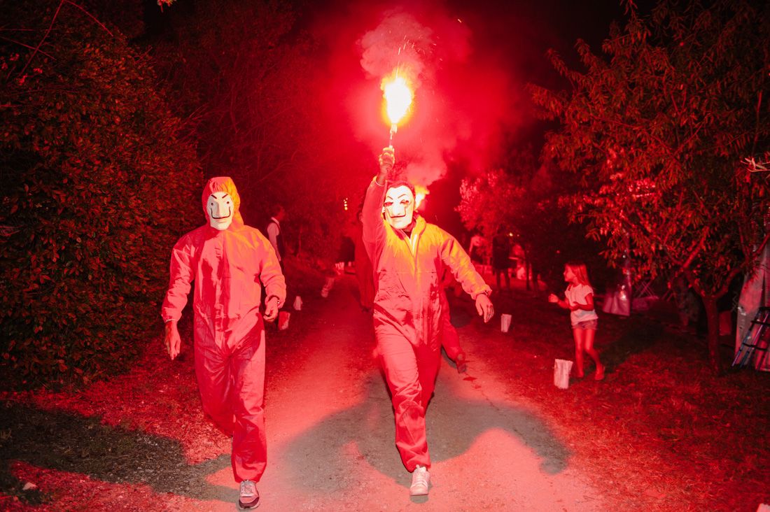 Two performers in red jumpsuits and masks running with flares at nighttime wedding event.
