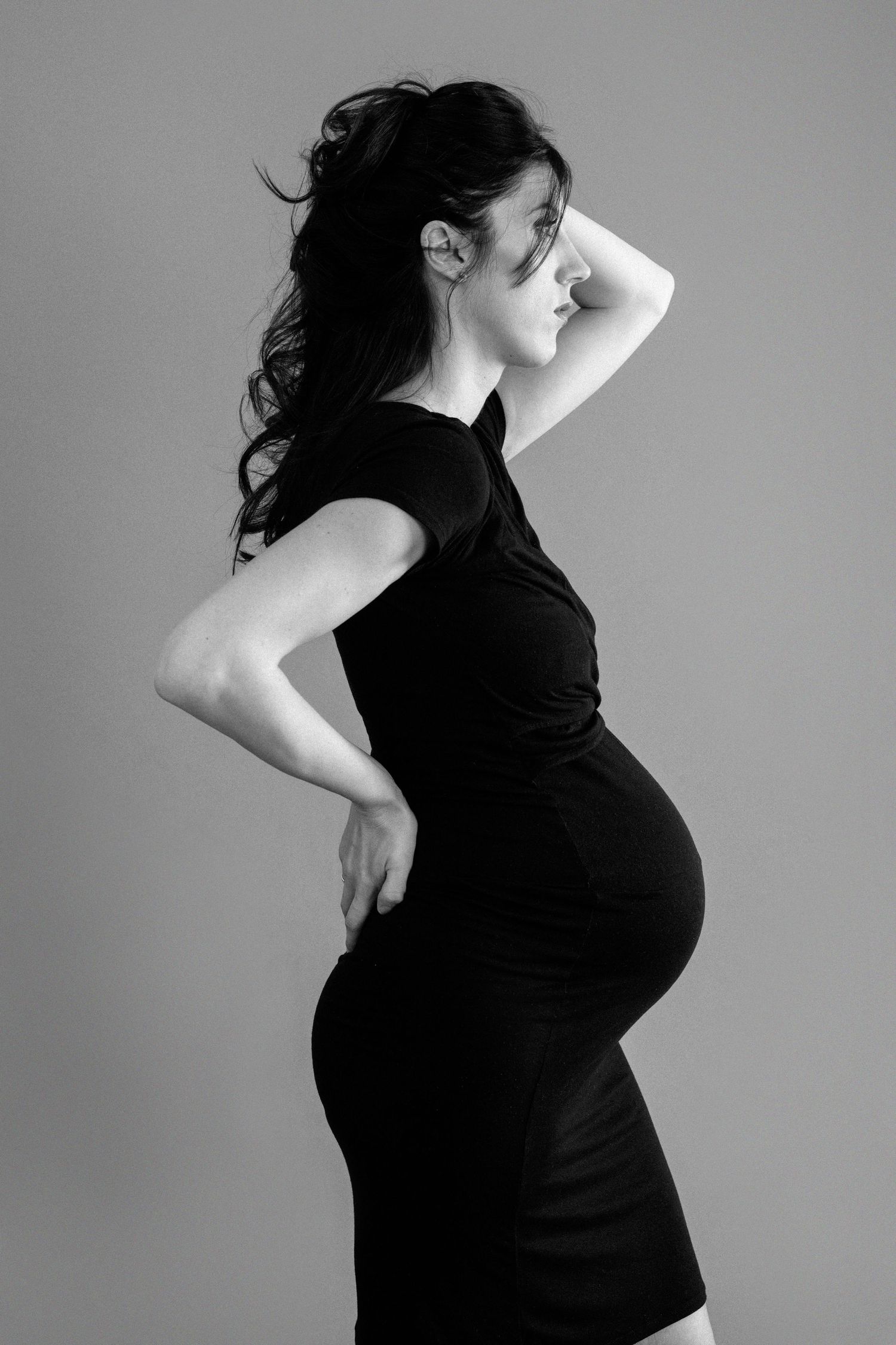 Black and white side profile of pregnant woman in black dress showcasing her baby bump.